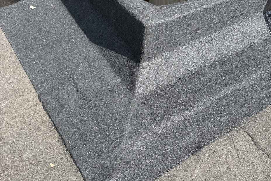 Torch-on mineral cap sheet dressed up an upstand and mitred at the external corner, lapped down onto the roof surface.