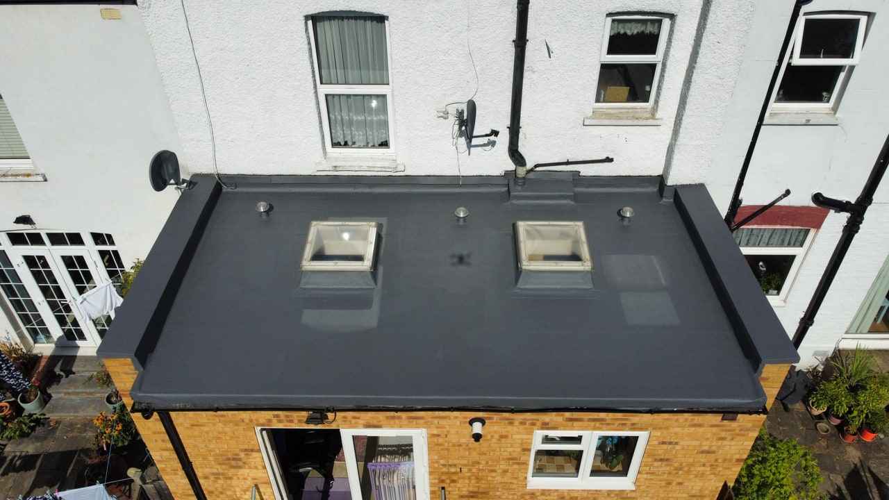 An existing felt roof renewed with a cold-applied liquid system, seen from above: one continuous surface dressed up to the parapet and over the edge, with two rooflight kerbs and three vents detailed in.