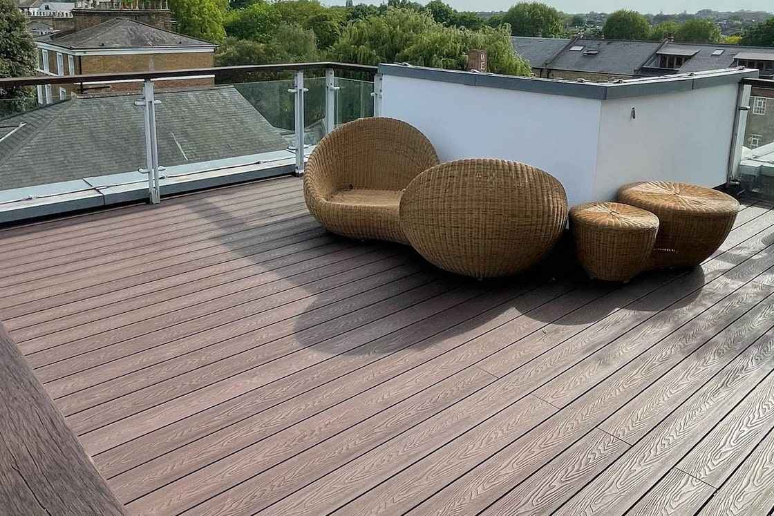 Composite decking laid over a waterproofed roof terrace, with a glass balustrade at the edge and a rendered parapet behind.